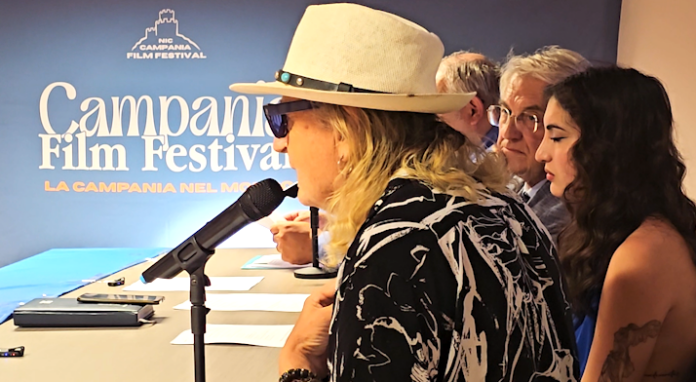 Foto della conferenza stampa del Campania Film Festival con persone sedute dietro a un tavolo con microfoni, davanti a uno sfondo con il logo del festival.