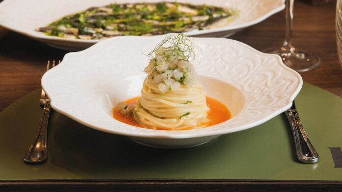 Piatto elaborato con spaghetti avvolti a forma di copricapo sulla salsa di pomodoro, guarnito con tartare di pesce e basilico, piatto decorato con effetto oro alimentare.
