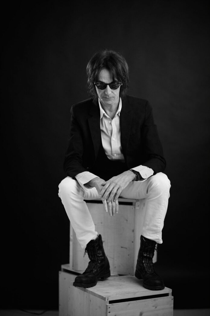 Ritratto artistico in bianco e nero di un uomo seduto con occhiali da sole e giacca, foto allegata al comunicato stampa.