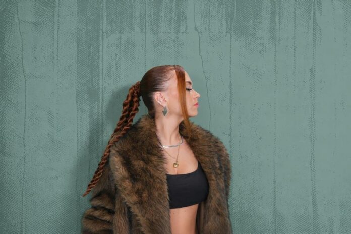 Ritratto di Stessy, cantante soul con vestito nero e giacca in pelliccia, sullo sfondo verde con scritte Lentamente, papik e stessy