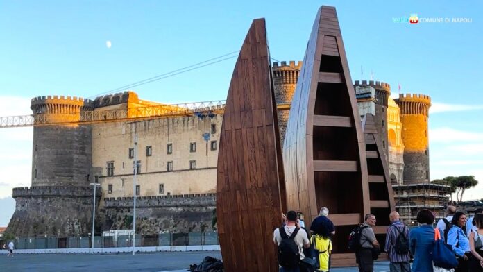 Tre barche in legno tradizionali ghanesi installate in piazza Municipio a Napoli con il castello sullo sfondo.