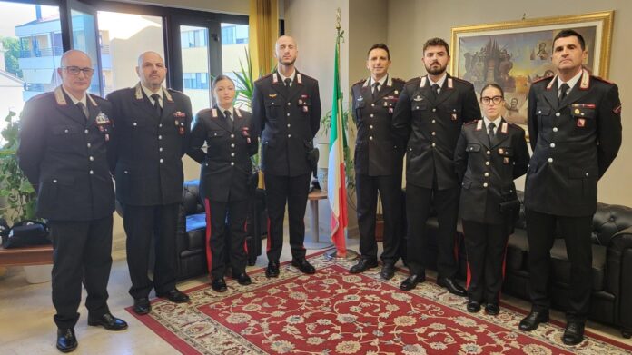 Gruppo di Carabinieri in divisa in un ambiente interno con bandiera italiana.