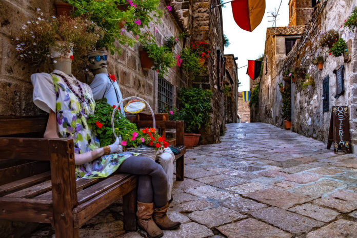 Via pietrosa del borgo di Casertavecchia con decorazioni colorate e manichini su una panchina.
