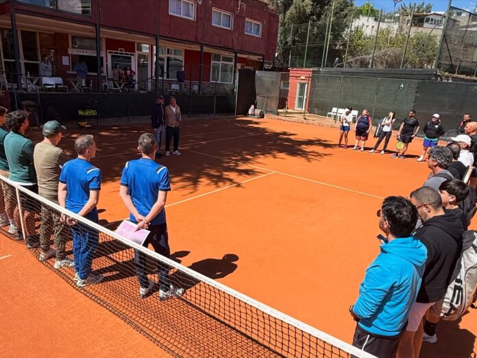 Campo da tennis in terra rossa con gruppo di persone riunite per una riunione o briefing.