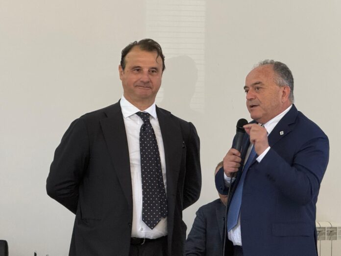 Delegazione istituzionale in visita al complesso agricolo Balzana con edifici in ristrutturazione e persone che camminano sul terreno esterno.
