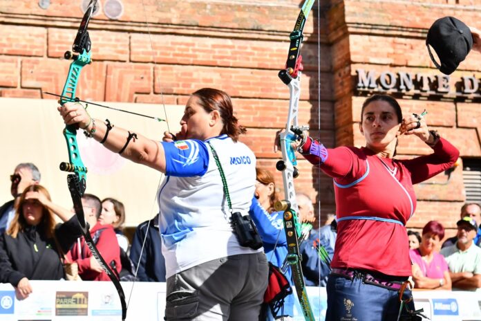 Arcieri durante una gara di tiro con l'arco con arco compound al momento dello scocco della freccia, in una competizione ufficiale con arco e bersagli visibili.