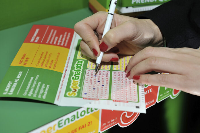 Mano che compila una schedina del SuperEnalotto con penna.