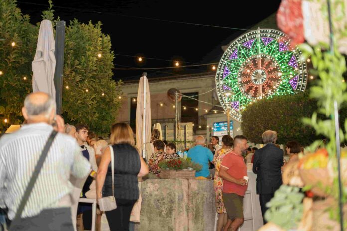 Persone sedute in cerchio in un incontro pubblico all'aperto con banner di 