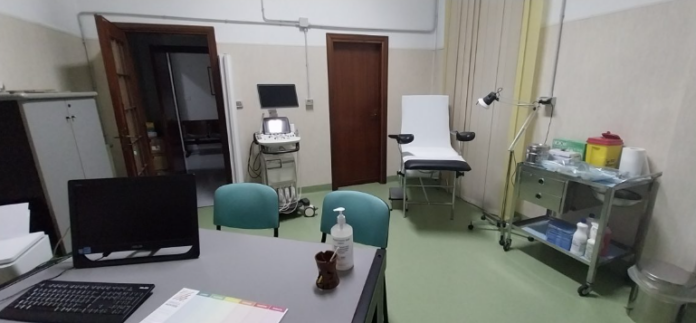 Interno del Centro Medico Sociale con scrivania, sedie, lettino medico e attrezzature in una stanza funzionante per visite.