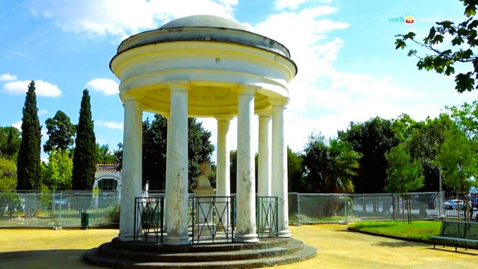 Struttura circolare con colonne nella Villa Comunale di Napoli, area verde con recinzioni per lavori in corso.