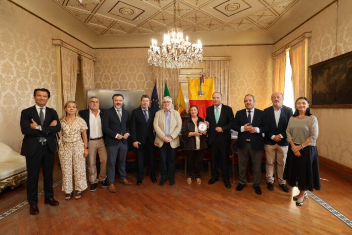 Gruppo di persone in un incontro ufficiale in una sala del Comune di Napoli con bandiere nazionali sullo sfondo
