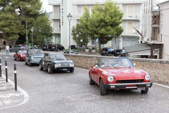 Auto d'epoca in sfilata su strada con persone e edifici storici sullo sfondo a Monteprandone.