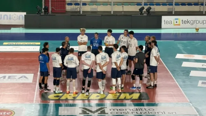 Giocatori e staff tecnico della Union Volley Napoli in cerchio sul campo da pallavolo durante una riunione tecnica.