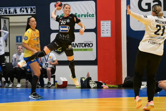 Giocatrice della Jomi Salerno in azione durante una partita di pallamano, con una portiera e un'avversaria visibili in campo.
