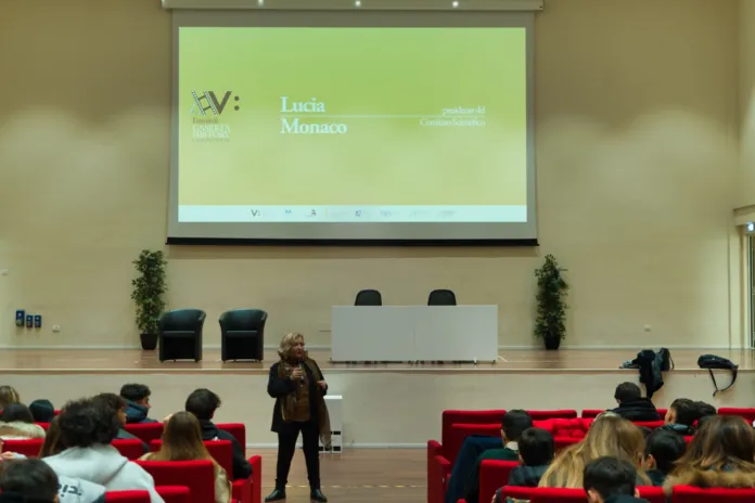 Una relatrice è davanti al pubblico in un’aula universitaria; sullo schermo è proiettata una presentazione.