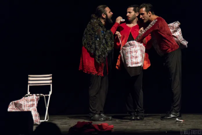 Tre interpreti in scena, raccolti attorno a borse di stoffa; sulla sinistra c’è una sedia.