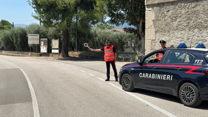 Carabiniere in alta visibilità che ferma un'auto durante un controllo stradale con veicolo dei Carabinieri parcheggiato a lato.