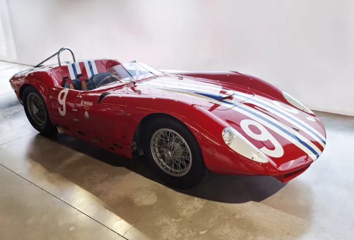 Vettura da corsa rossa con numero 9 e strisce blu e bianche, esposta in un ambiente interno.