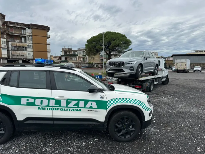 Auto Volvo XC60 grigia su carrello con fianco di una volante della Polizia Metropolitana di Napoli in un parcheggio.