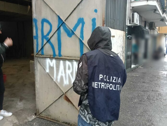 Poliziotto della Polizia Metropolitana di Napoli davanti a un cancello con scritta marmo, immagine di archivio dell'attività di controllo.