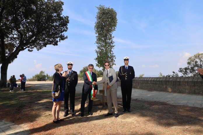 Un gruppo di persone in piedi intorno a un albero appena piantato nel Parco Virgiliano, con cielo limpido sullo sfondo.