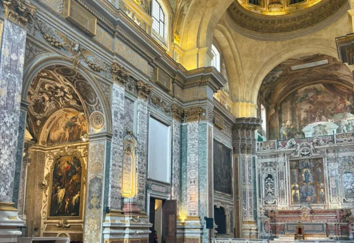 Navata di una chiesa con colonne decorate, dipinti e altare.