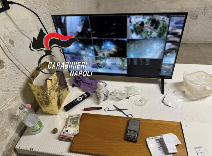 Monitor con immagini di sorveglianza, denaro, bilancia di precisione e altri oggetti su un tavolo in un ambiente chiuso.