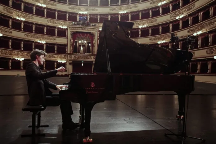 Immagine di archivio di un concerto di musica classica in un teatro, con un pianista seduto al pianoforte sul palco.