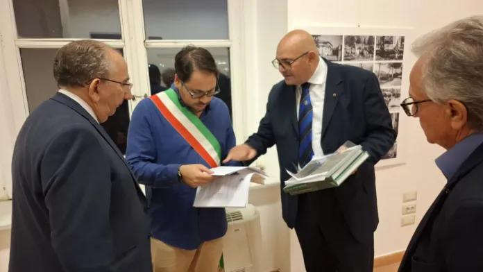 Immagine di archivio raffigurante un momento di firma di un accordo ufficiale, con realtà di persone sedute a un tavolo, alcune con cappelli tricolori, durante un evento formale.