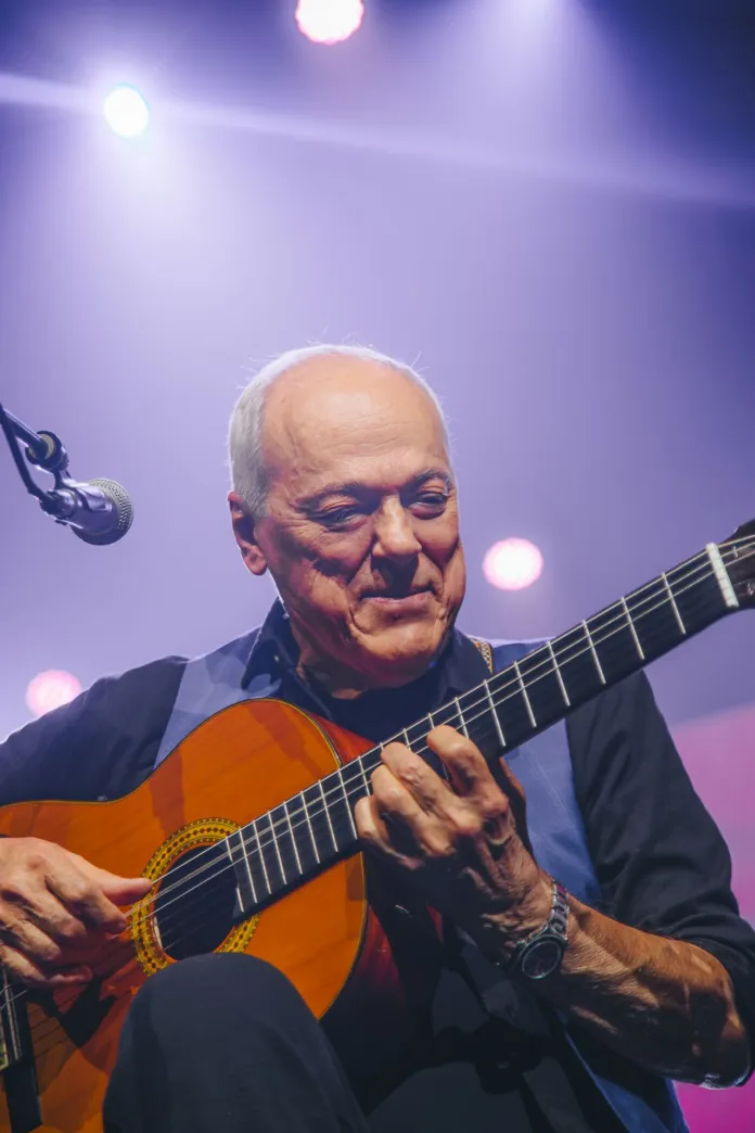 Immagine di un concerto di Toquinho con luci colorate sul palco, mostra il musicista che suona la chitarra