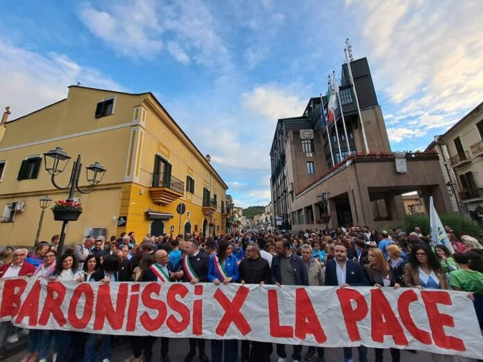 Manifestazione a Baronissi con persone che tengono uno striscione con scritto BARONISSI X LA PACE, evento legato al Festival della Pace.