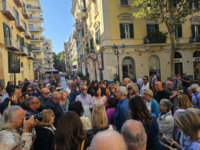 Foto di un gruppo numeroso di persone radunate in una via di Napoli durante un evento culturale all'aperto.
