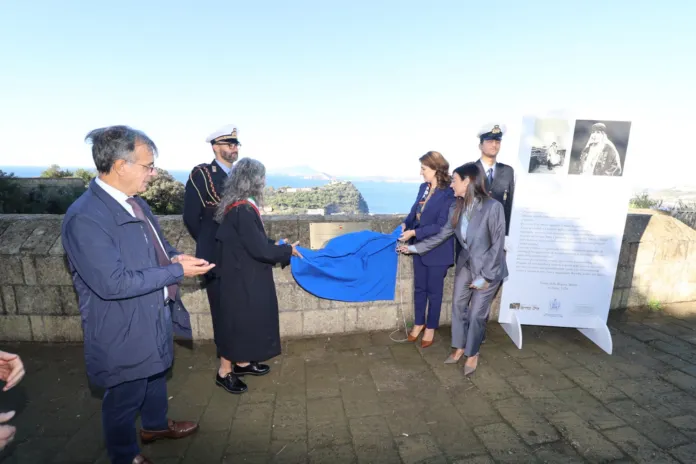 Cerimonia con persone che scoprono una targa commemorativa all'aperto, sullo sfondo mare e paesaggio