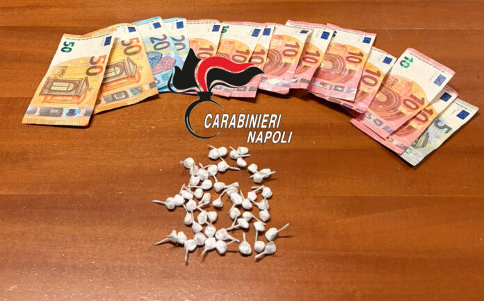 Dosi di droga e banconote in euro disposte su un tavolo con il logo dei Carabinieri di Napoli.