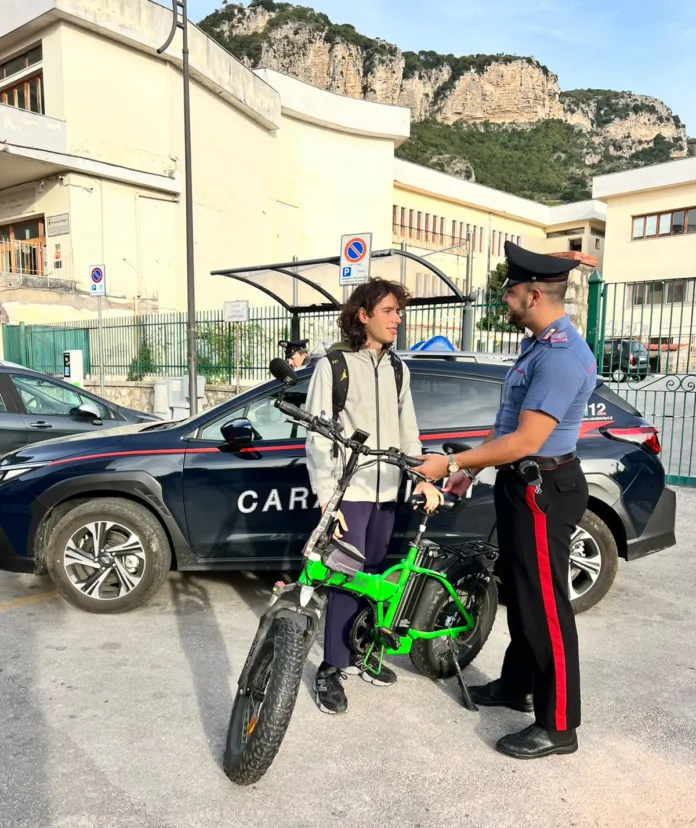 Foto illustrativa di un carabinieri che controlla un ragazzo con una bicicletta elettrica, scena urbana.