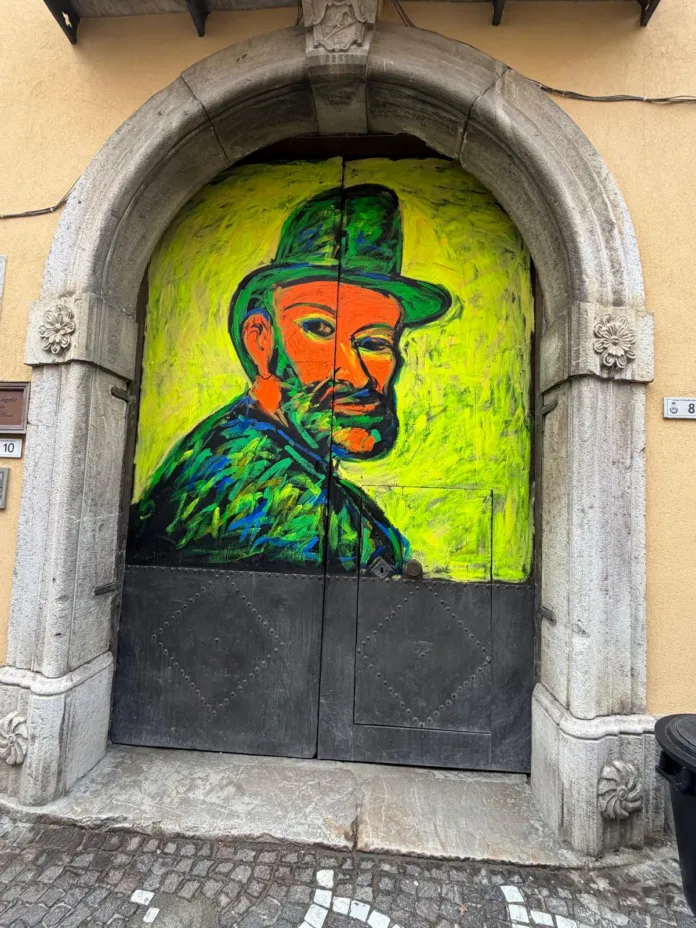 Un portone ad arco con le ante dipinte di verde e giallo e un ritratto con cappello.