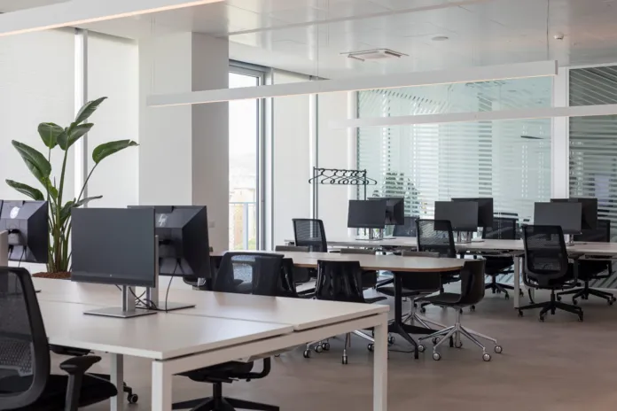 Postazioni di lavoro con scrivanie, monitor e sedie in un ufficio luminoso.