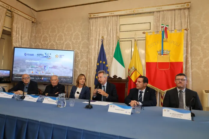 Persone sedute a un tavolo in una sala; sullo schermo alle loro spalle compare una grafica sul judo.