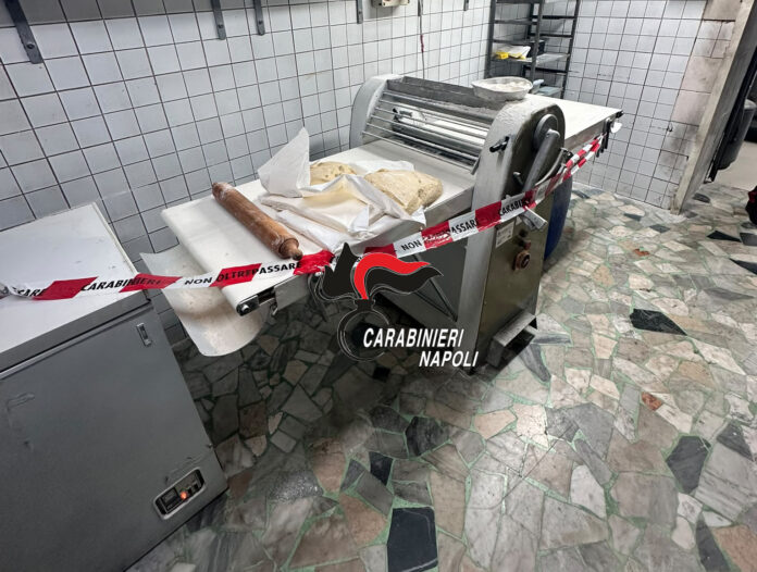 Laboratorio di pasticceria con macchina e tavolo sigillati dal nastro dei Carabinieri a Napoli.