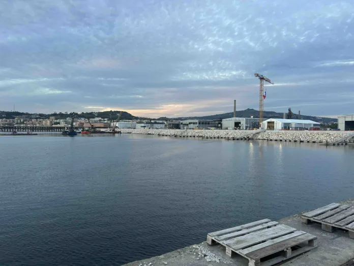 Specchio d’acqua in primo piano; oltre una banchina si vedono un edificio e una gru.