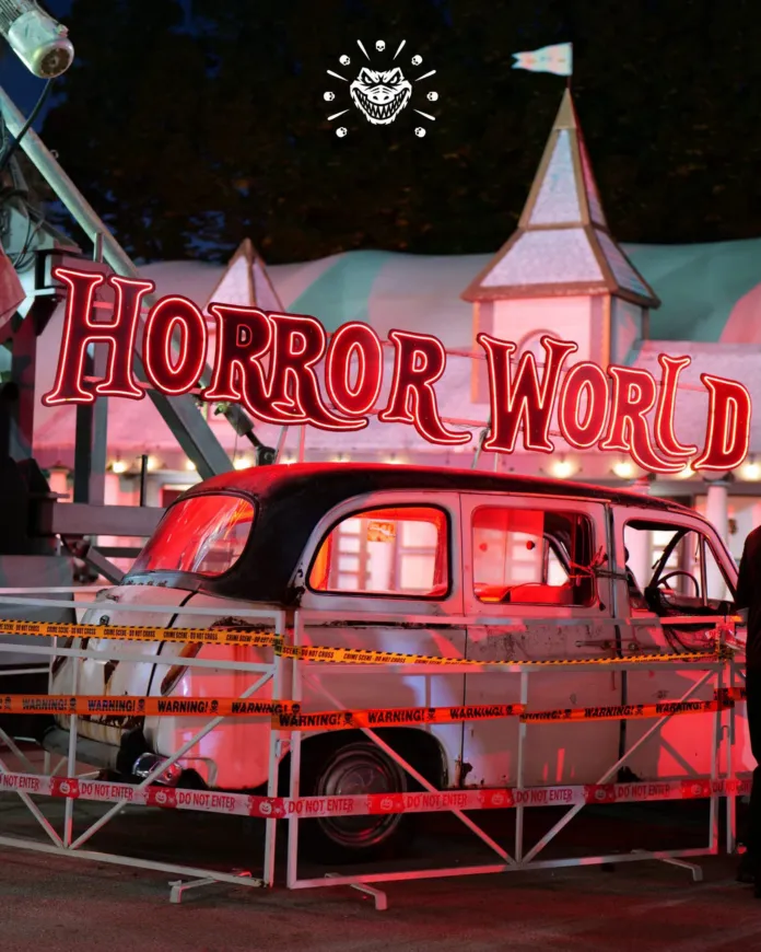 Insegna luminosa “Horror World” sopra un’automobile scenografica, delimitata da transenne.