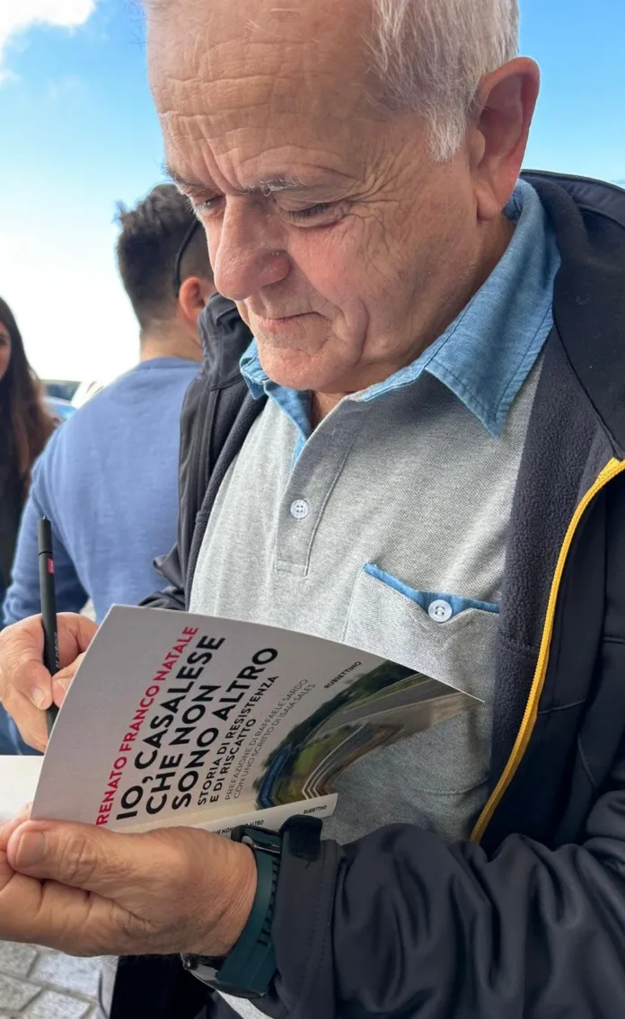 Una persona sfoglia il libro “Io, casalese che non sono altro”, con altre persone sullo sfondo.