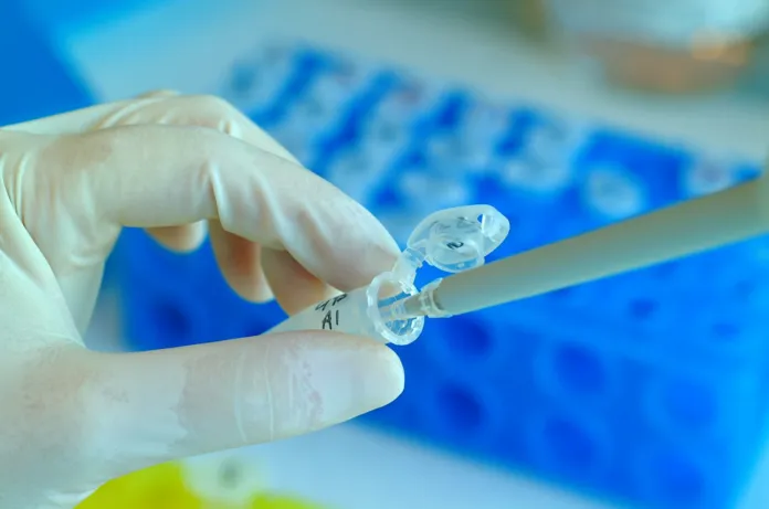 Mano con guanto protettivo che utilizza una pipetta per transferire liquido in laboratorio.