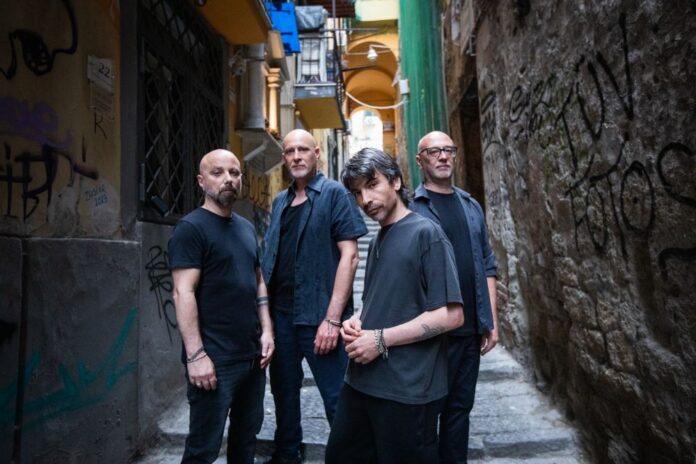 La band 24 Grana in una strada stretta con graffiti sui muri.