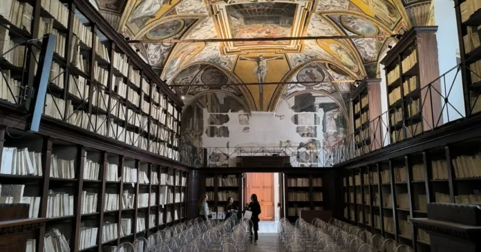 Interno dell'Archivio di Stato di Napoli con scaffali di libri e scaffalature alte, sala con soffitto affrescato e sedie trasparenti.