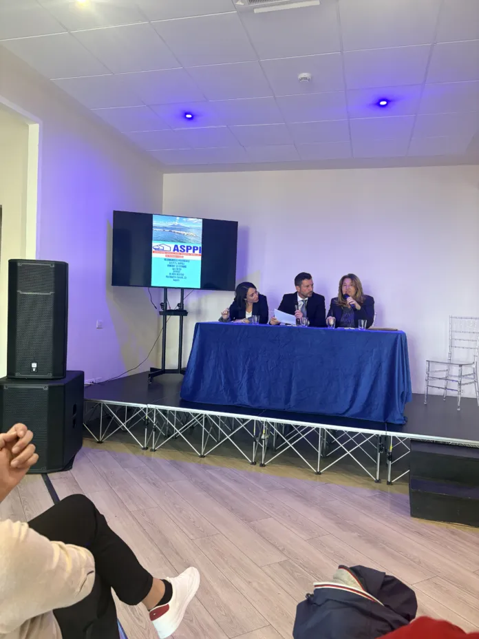 Fotografia di un congresso o riunione con partecipanti seduti a un tavolo e uno schermo con logo ASPPI sullo sfondo.