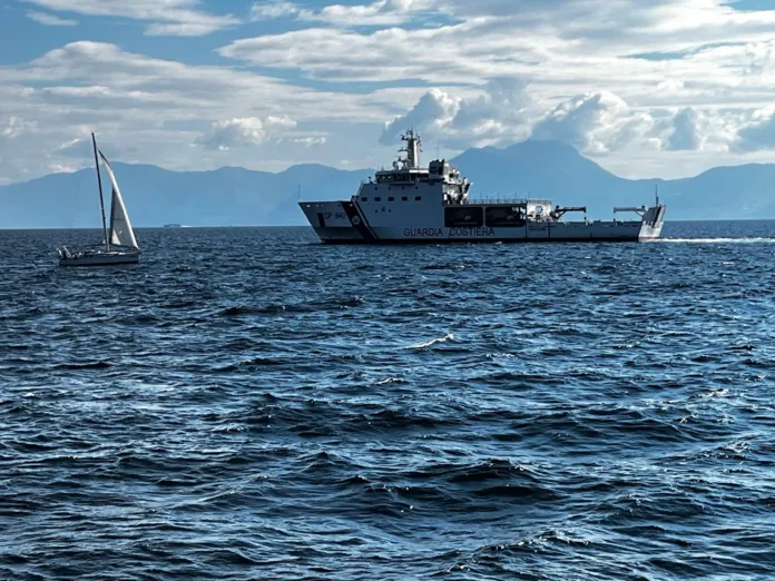 Una nave con la scritta «Guardia Costiera» naviga accanto a una barca a vela.