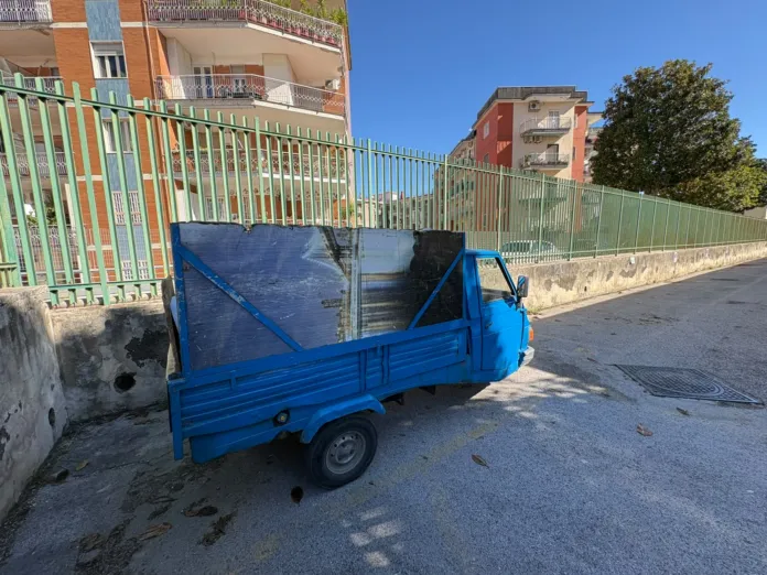 Motoveicolo blu simile a quello sequestrato per trasporto illecito di rifiuti ad Arzano, parcheggiato in strada davanti a una recinzione verde.