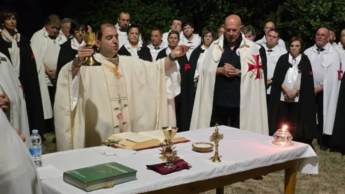 Un sacerdote celebra davanti a un gruppo di persone in tuniche bianche, raccolte attorno a un altare con calice e altri oggetti liturgici.