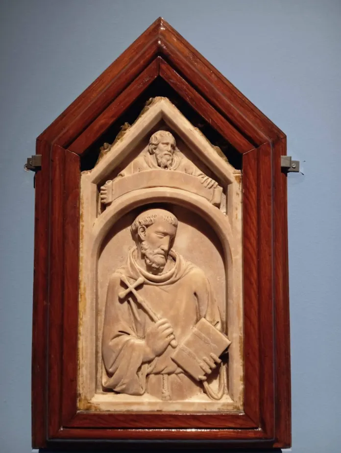 Rilievo in marmo con la figura di un frate che regge una croce e un libro, inserito in una cornice lignea.